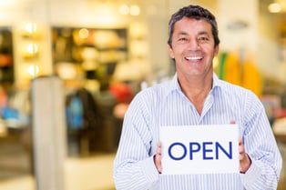 Male business owner holding an open sign and smiling